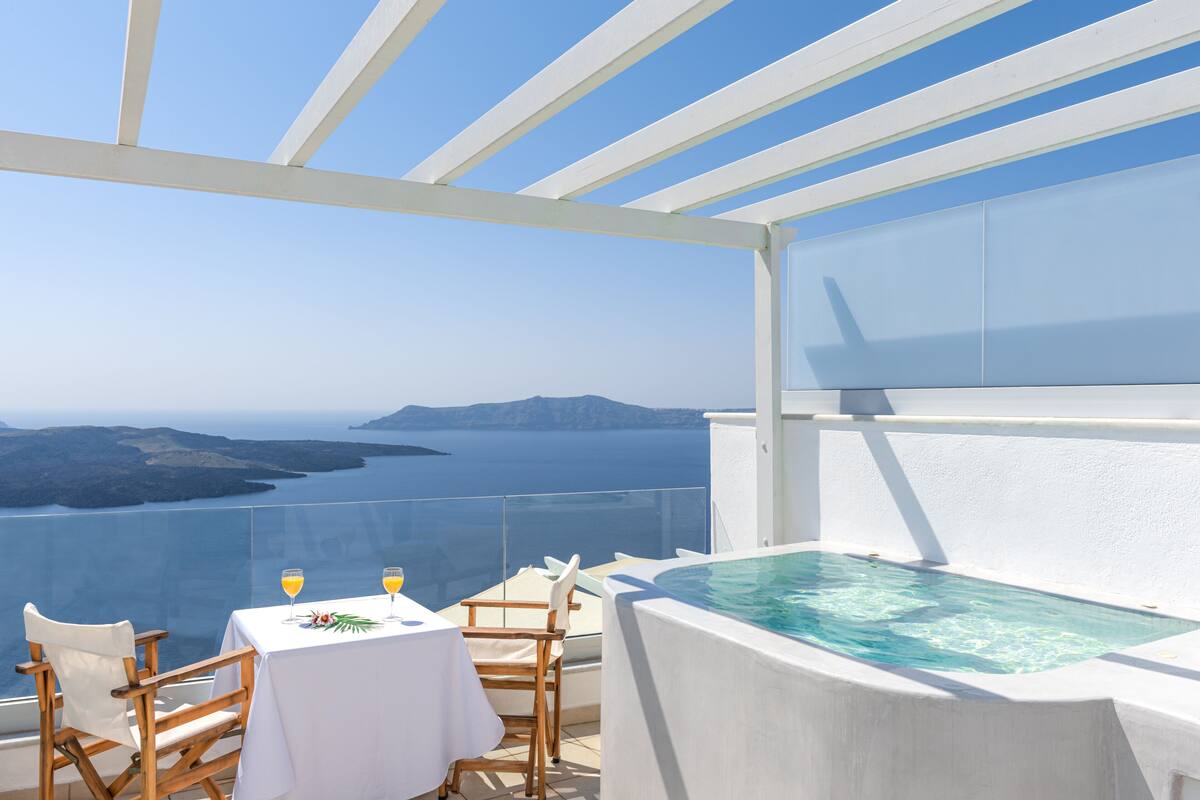 Une terrasse avec une piscine, une table à manger, des chaises et une vue sur la mer et les îles.