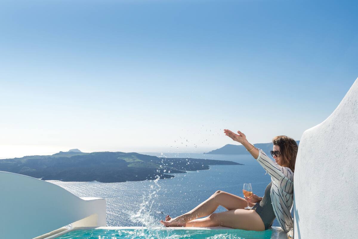 Une personne se détend au bord d’une piscine, avec une vue dégagée sur la mer et les collines lointaines.