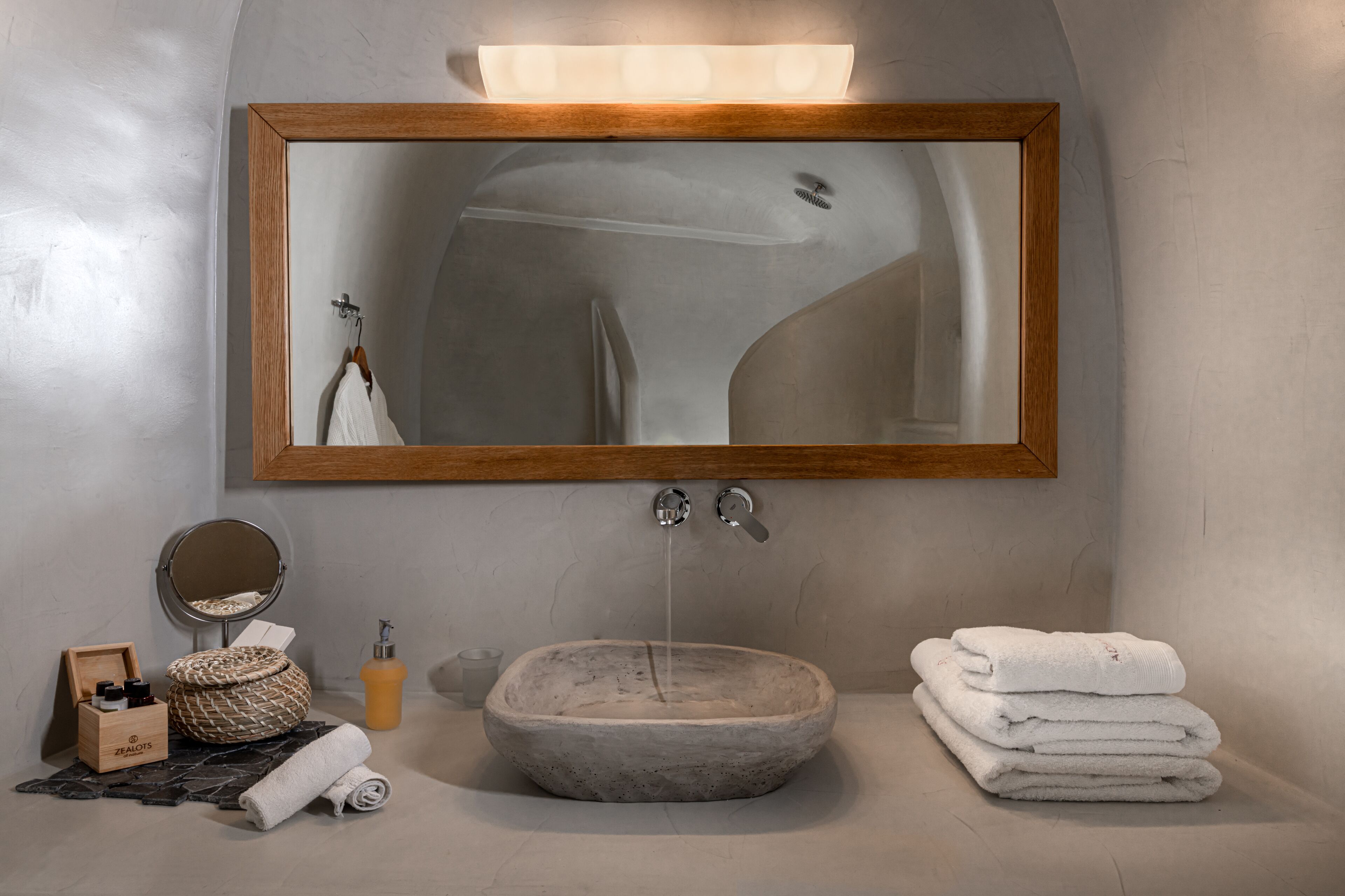 A bathroom with a wooden-framed mirror, a stone sink, and a towel stack.