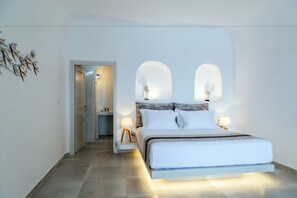 Ett modernt sovrum med en stor säng, två sänglampor och en dörr som leder till ett badrum.