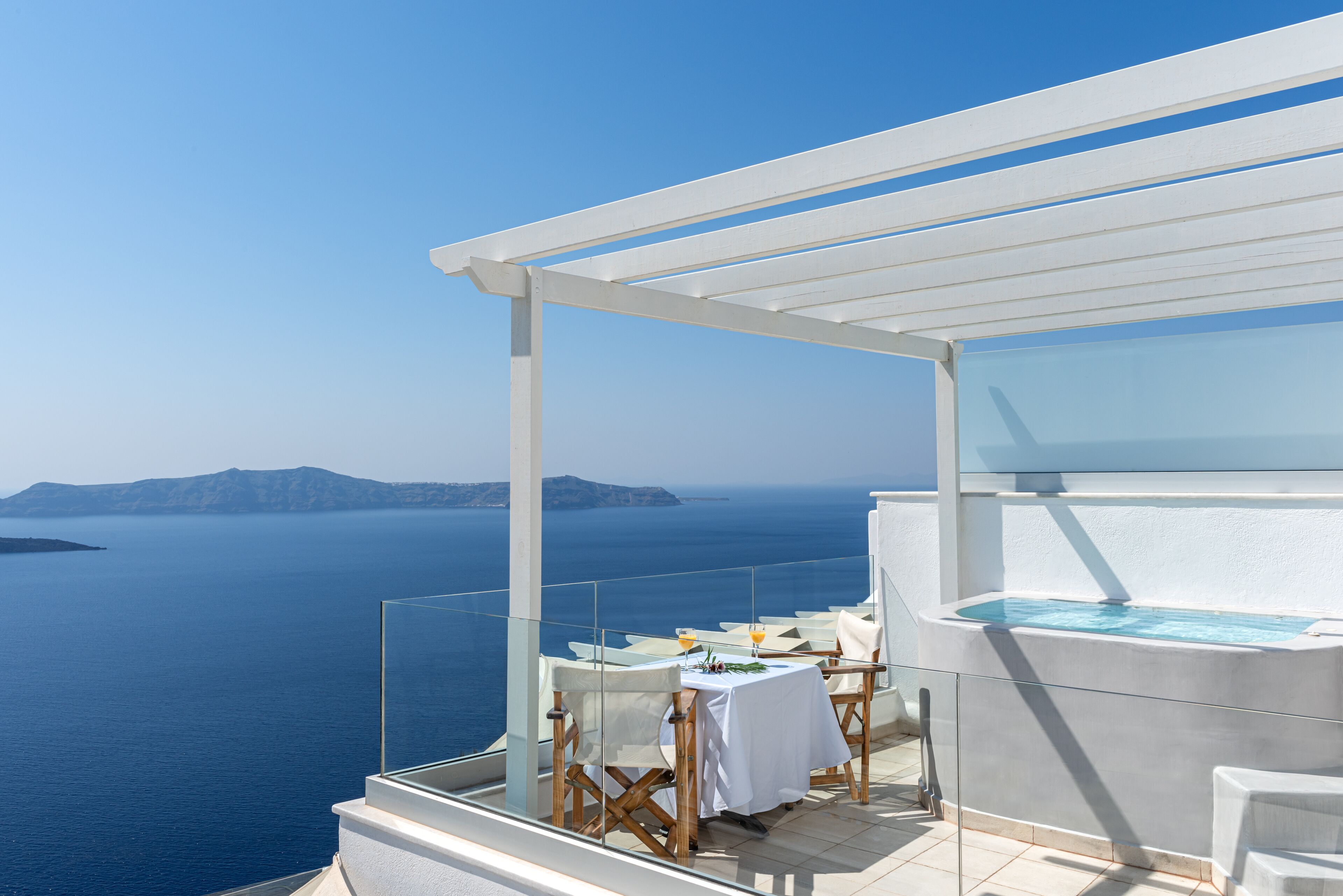 A balcony with a table set for two, overlooking a body of water and distant landforms.
