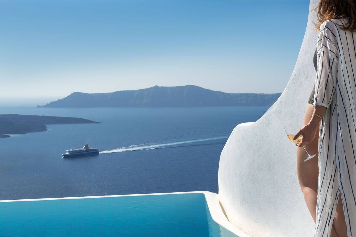 Une personne se tient près d’une piscine, avec vue sur un navire de croisière sur l’eau et sur des montagnes lointaines.