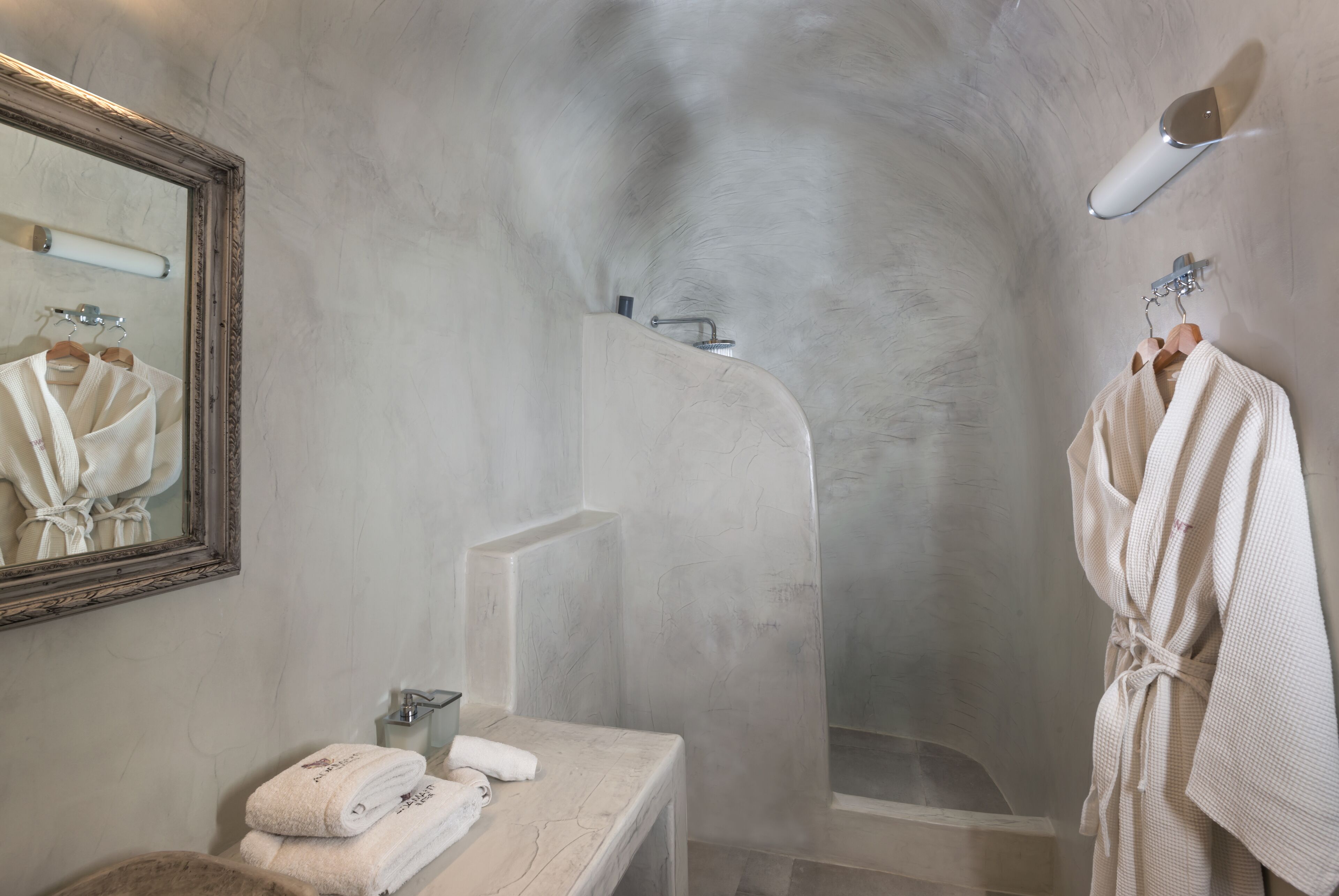 A bathroom with a marble vanity, a large mirror, a shower with a curved wall, and a robe hanging on a rack.