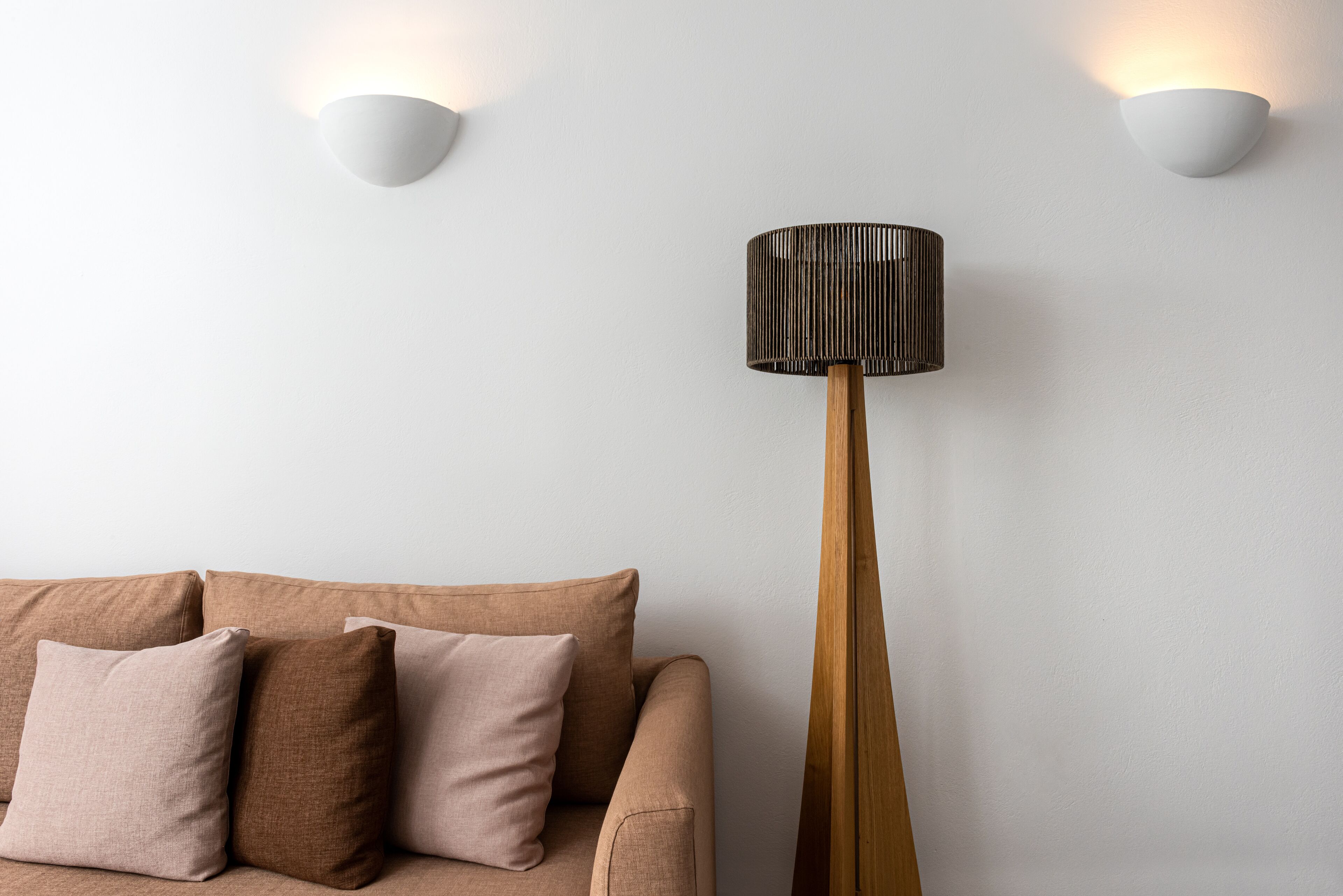 A modern living room with a beige sofa, three cushions, and a tall floor lamp with a cylindrical shade.