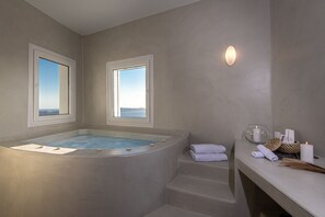 Ett spa-rum med ett bubbelbad, två fönster, en trappa och en avställningsyta med handdukar och ljus.