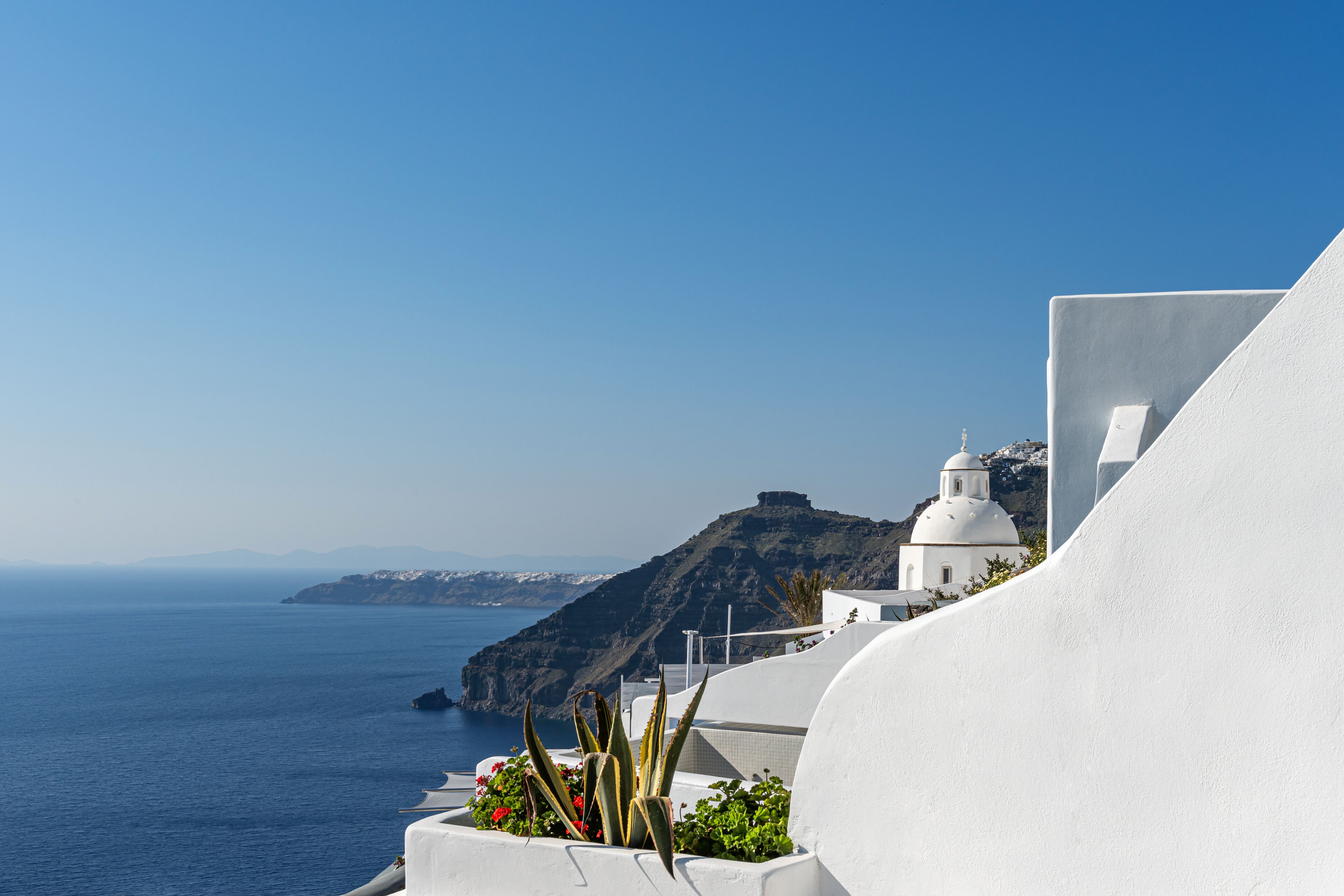 A white building with a dome and a flat roof, overlooking a body of water and a mountainous landscape.
