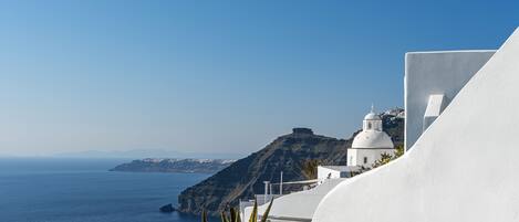 A white building with a dome and a flat roof, overlooking a body of water and a mountainous landscape.