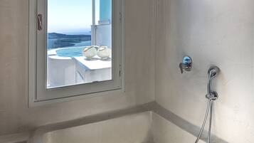 A bathroom with a bathtub, a shower, and a window offering a view of the sea.