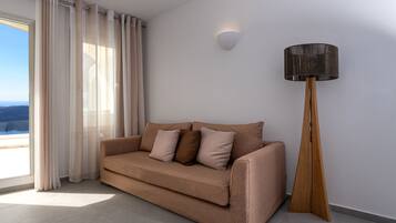 A modern living room with a beige sofa, a tall floor lamp, and a view through a large window.