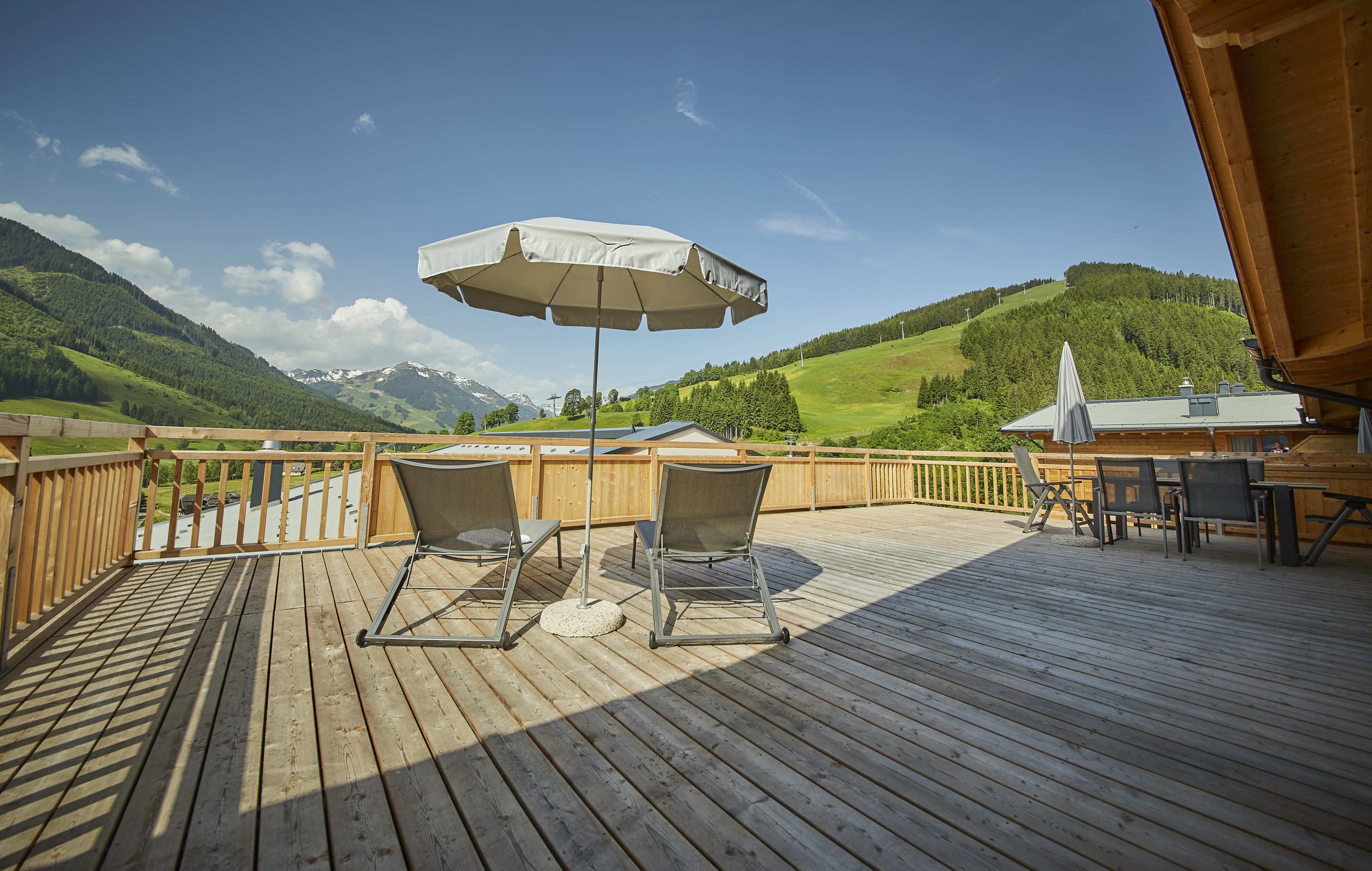 A wooden deck with two chairs and an umbrella, overlooking a mountainous landscape.