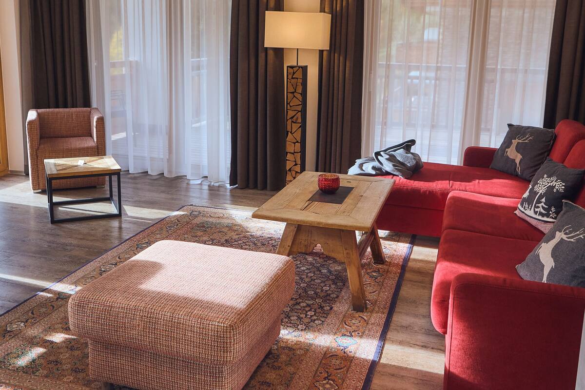 A living room with a red sofa, a red armchair, a wooden coffee table, and a patterned rug.