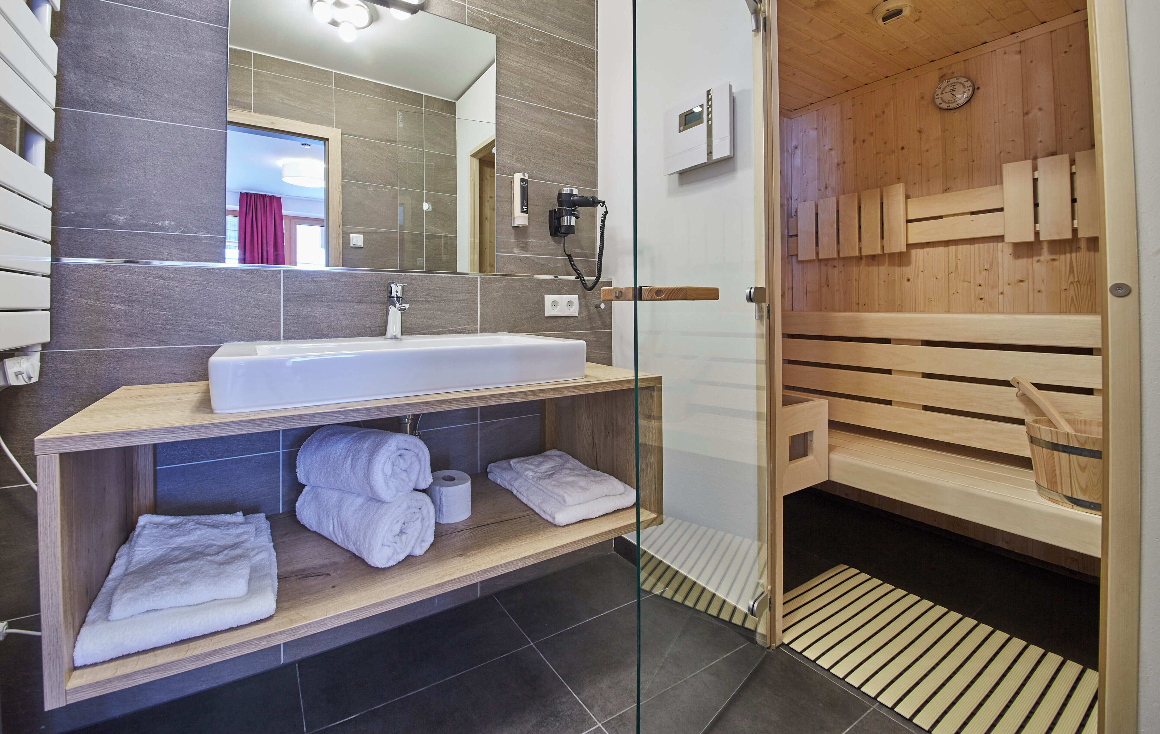 Een moderne badkamer met een ruime wastafel, spiegel en houten sauna.