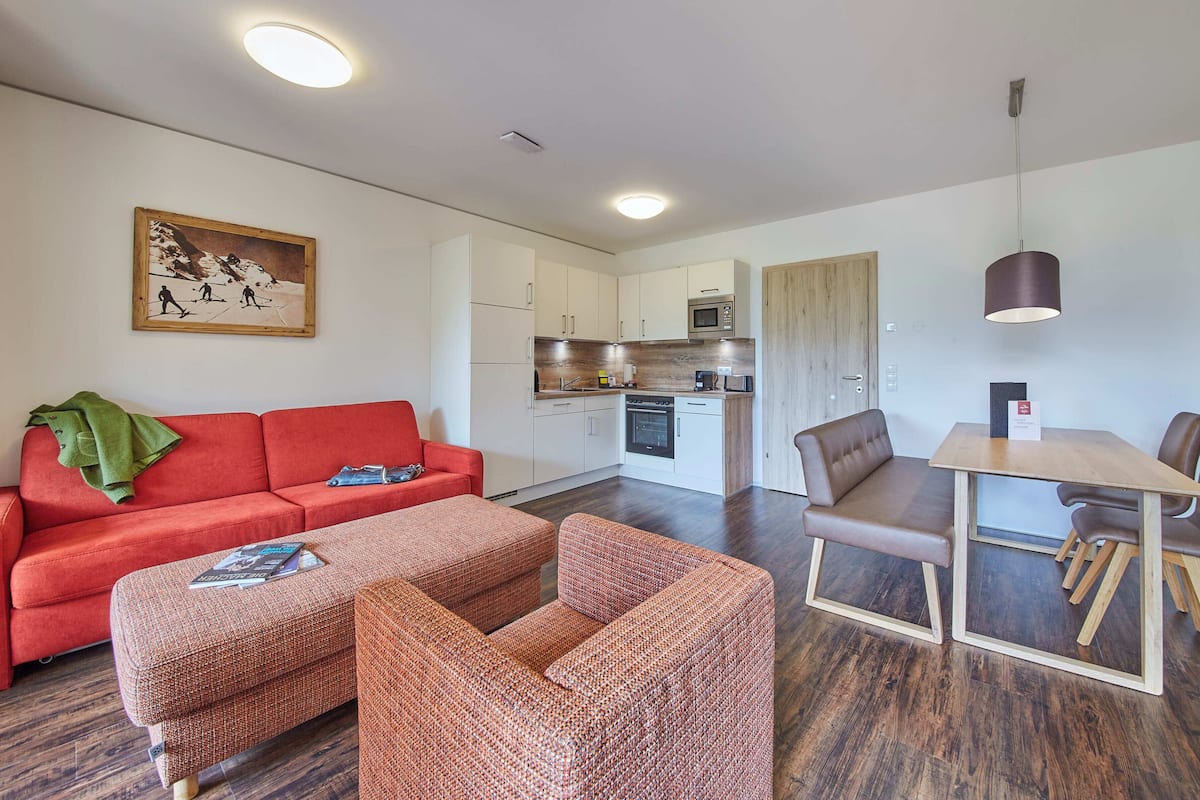 A compact living space with a kitchenette, a dining area, and a red sofa.