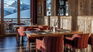 Un restaurant aux murs en bois et aux grandes fenêtres donnant sur une montagne enneigée. Les tables sont dressées avec des chaises à rayures rouges et de beaux couverts.