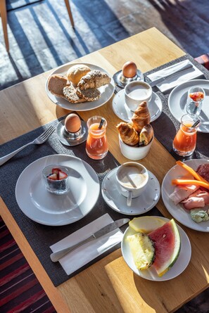 A breakfast table with croissants, eggs, juice, coffee, strawberries, and watermelon. - AlpenParks Hotel & Apartment Sonnleiten (Saalbach-Hinterglemm)