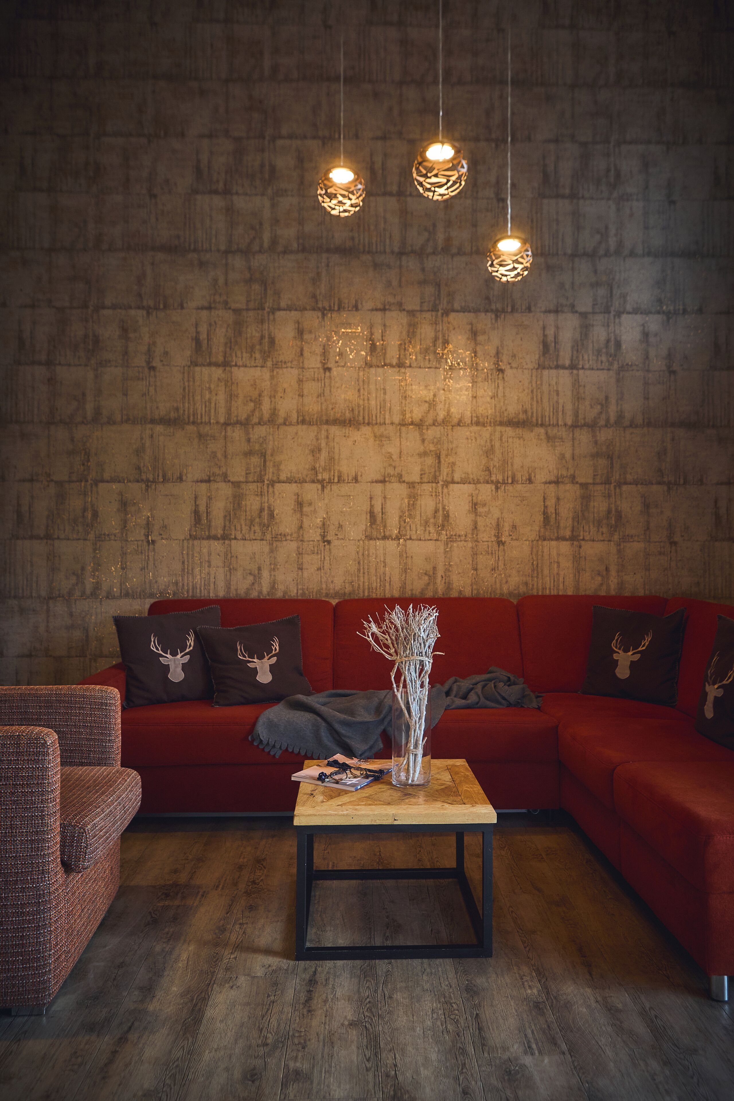 Una sala de estar acogedora con un sofá rojo, dos almohadones decorativos con motivos de ciervo, una mesa de centro de madera y lámparas colgantes.