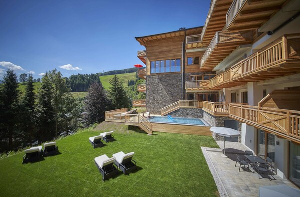A multi-story building with wooden balconies, a swimming pool, and outdoor seating. - AlpenParks Hotel & Apartment Sonnleiten (Saalbach-Hinterglemm)