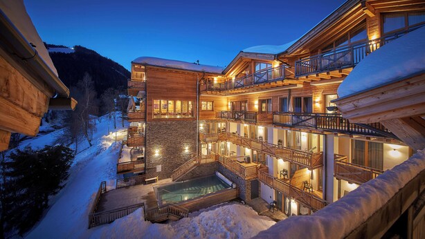 Un bâtiment en bois à plusieurs étages, doté de balcons, d’une piscine et entouré d’un paysage enneigé.