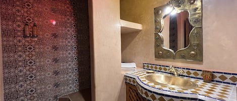 Une salle de bain avec des carreaux décoratifs, un lavabo agrémenté d’un miroir ornemental et un porte-serviettes.
