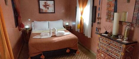 Une chambre d’hôtel comprenant un lit, une table de chevet, une commode, un luminaire au plafond et un climatiseur fixé au mur.