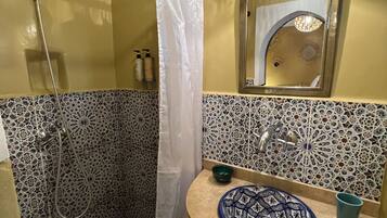 Un baño con ducha, lavabo con un cuenco decorativo y espejo con lámpara.