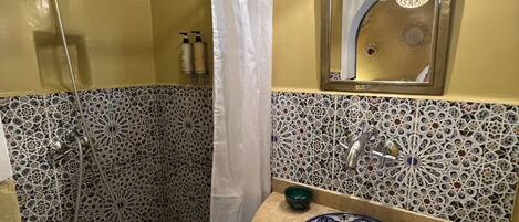 Un baño con ducha, lavabo con un cuenco decorativo y espejo con lámpara.