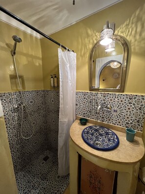 A bathroom with a shower, a sink with a decorative bowl, and a mirror with a light fixture.