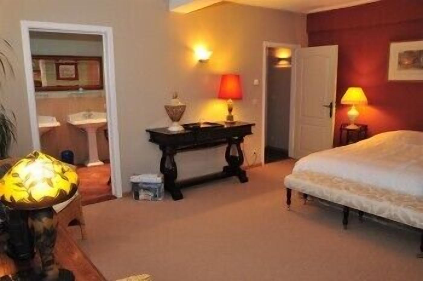 A hotel room with a bed, bedside table, lamp, and a view of the bathroom.