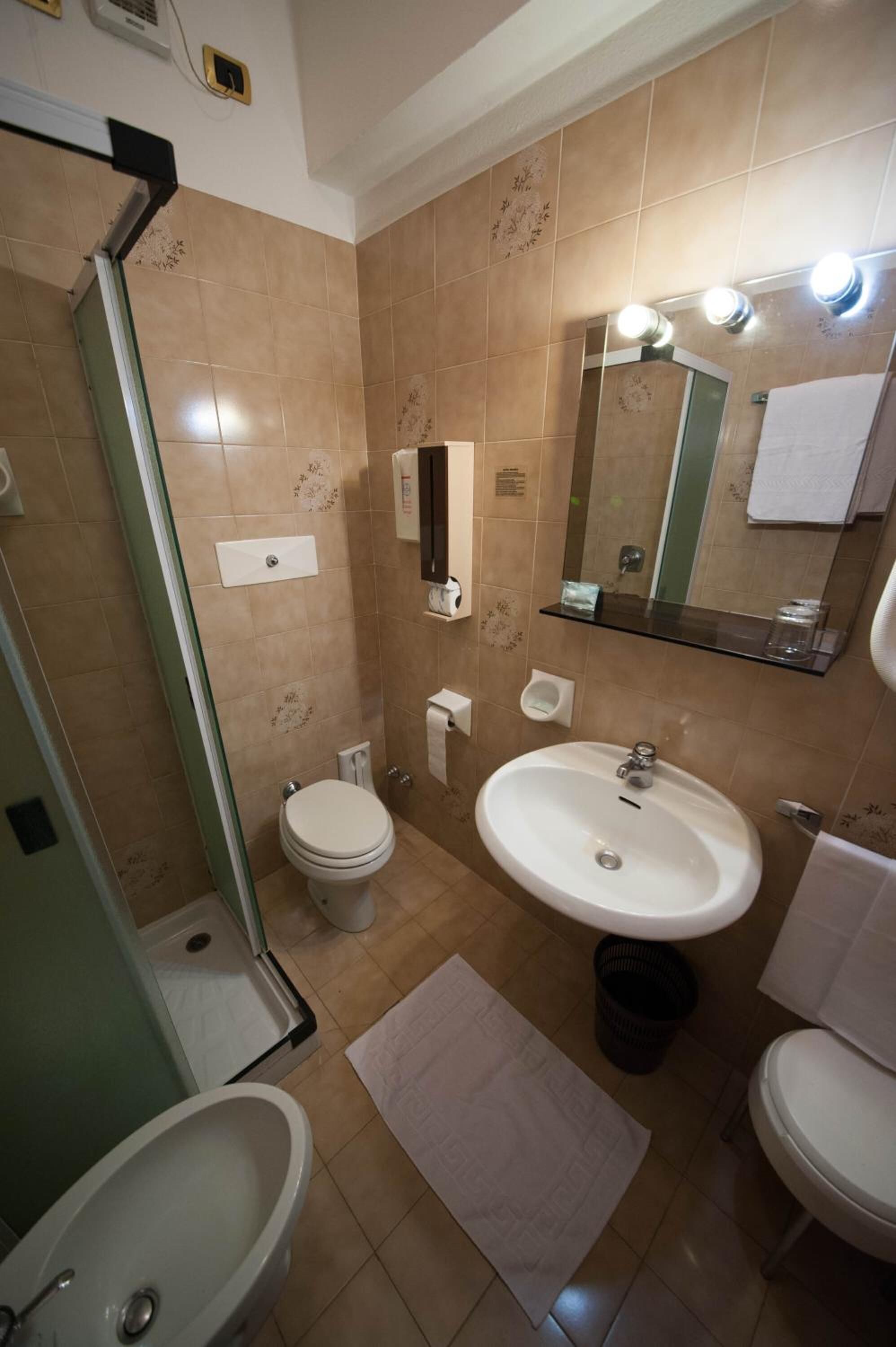 Un baño con cabina de ducha de vidrio, inodoro, lavamanos y espejo.