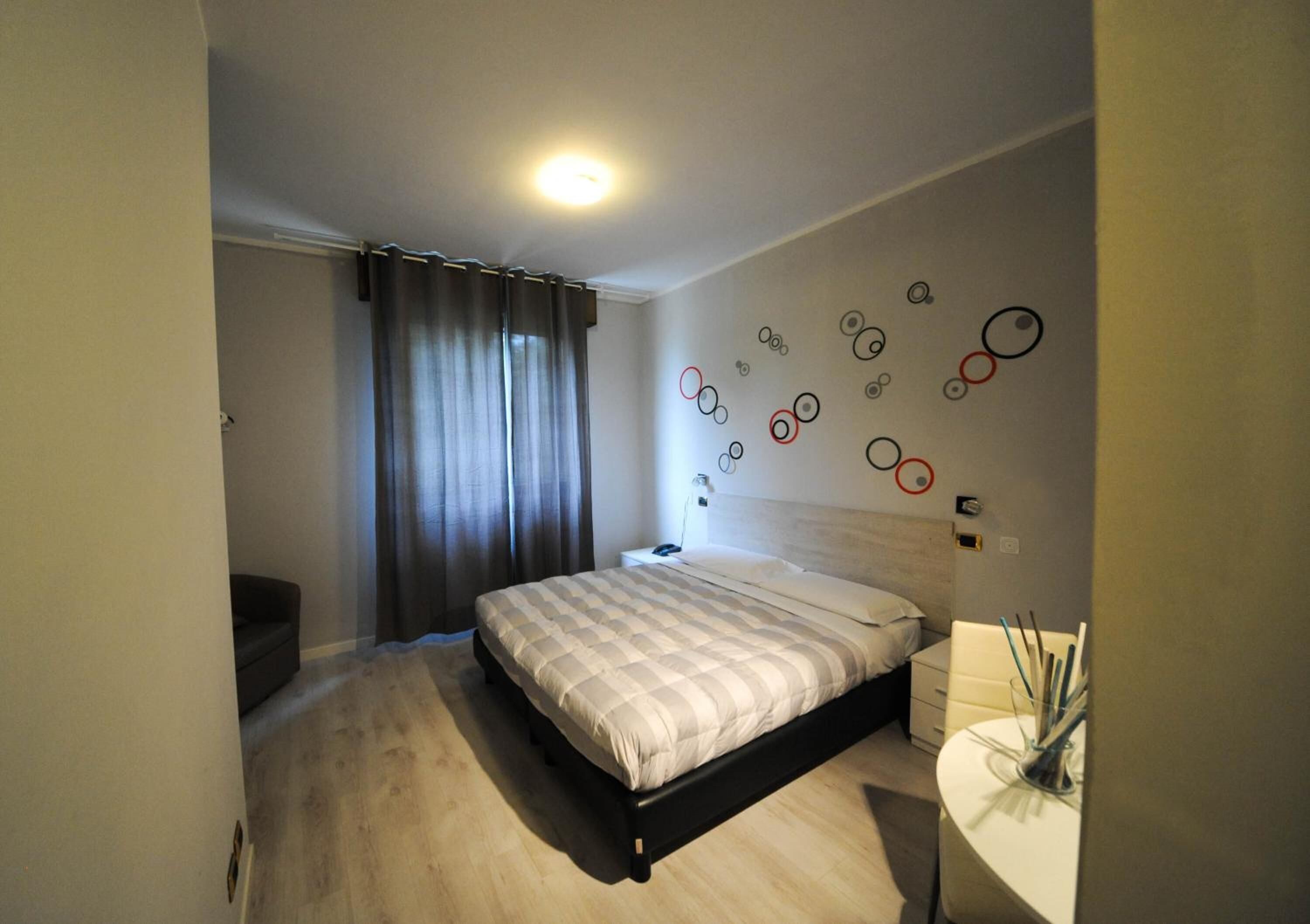Ein Schlafzimmer mit einem Bett, einem Nachttisch, einer Wand mit runden Dekorationen und einem Fenster mit Vorhängen.