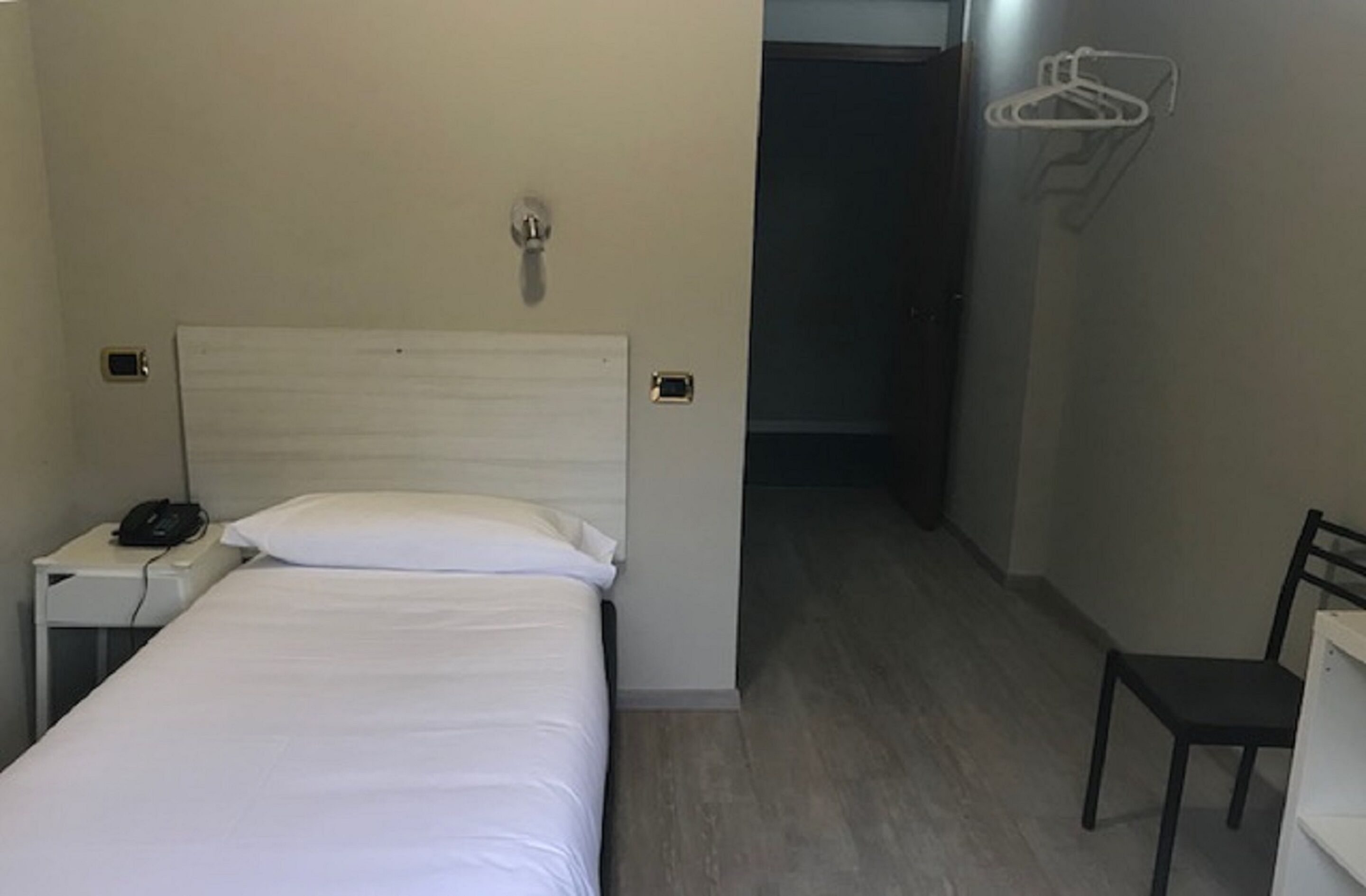 Una habitación de hotel con una cama, una mesita de noche con un teléfono, una silla y un perchero.