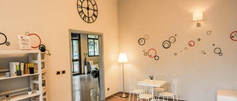 Une pièce avec une table et des chaises blanches, une horloge au mur et une bibliothèque.
