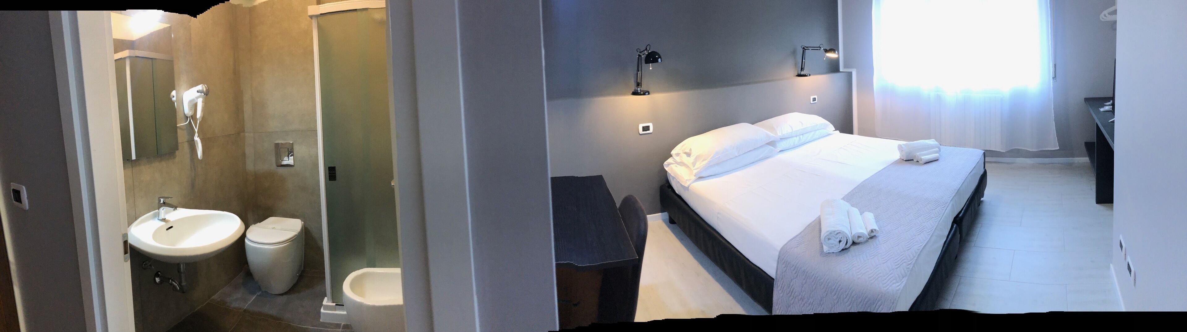 Una habitación de hotel con cama, mesita de noche, lámpara y baño completo.