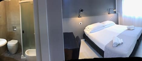 A hotel room with a bed, bedside table, lamp, and a bathroom with a sink and toilet.