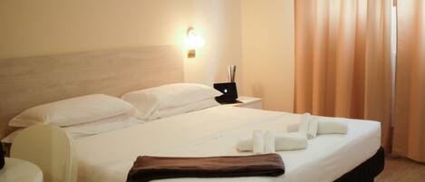 A hotel room with a bed, a nightstand, a chair, and a wall-mounted lamp.