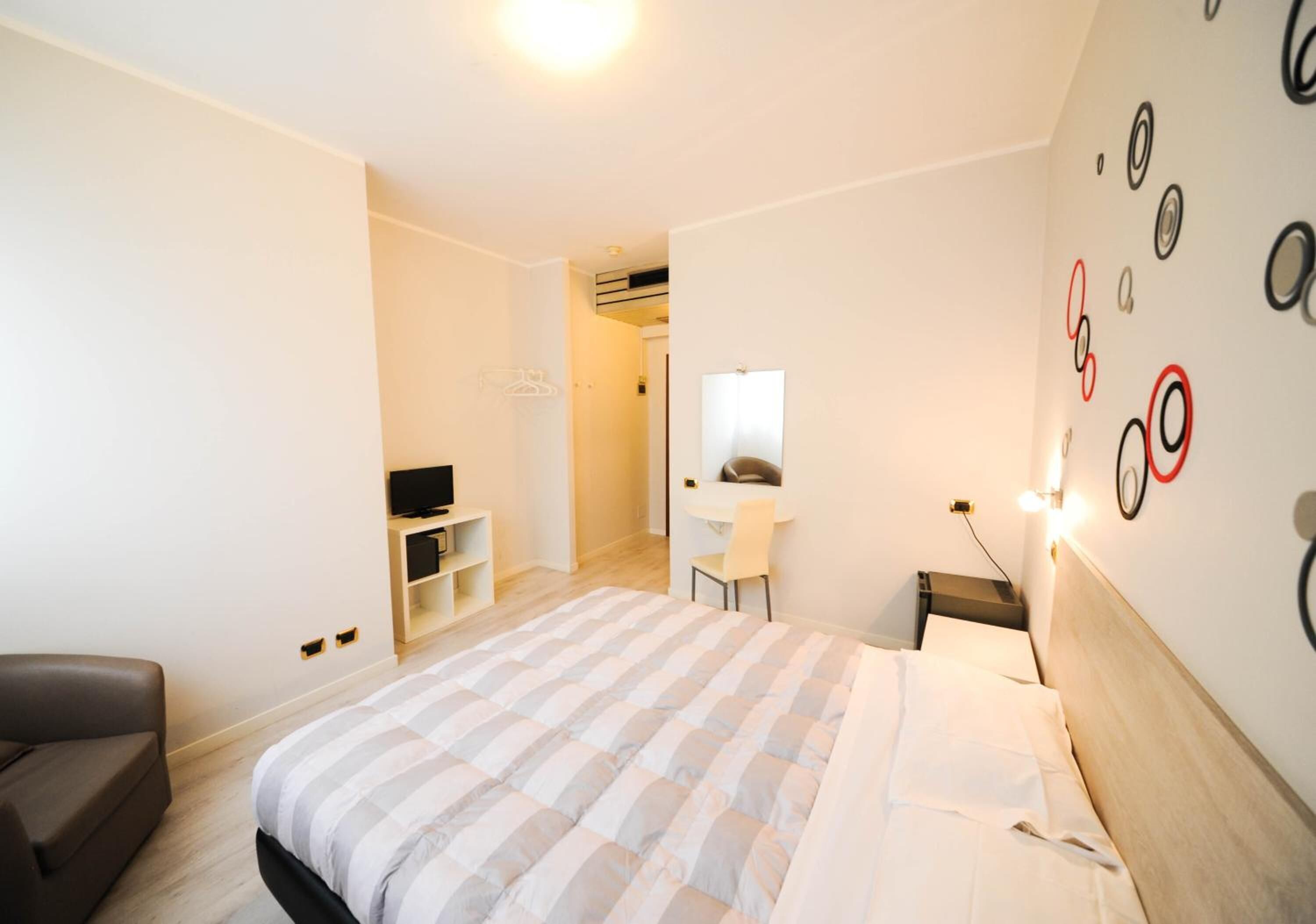 A modern hotel room with a large bed, a desk, a TV, and a wardrobe.