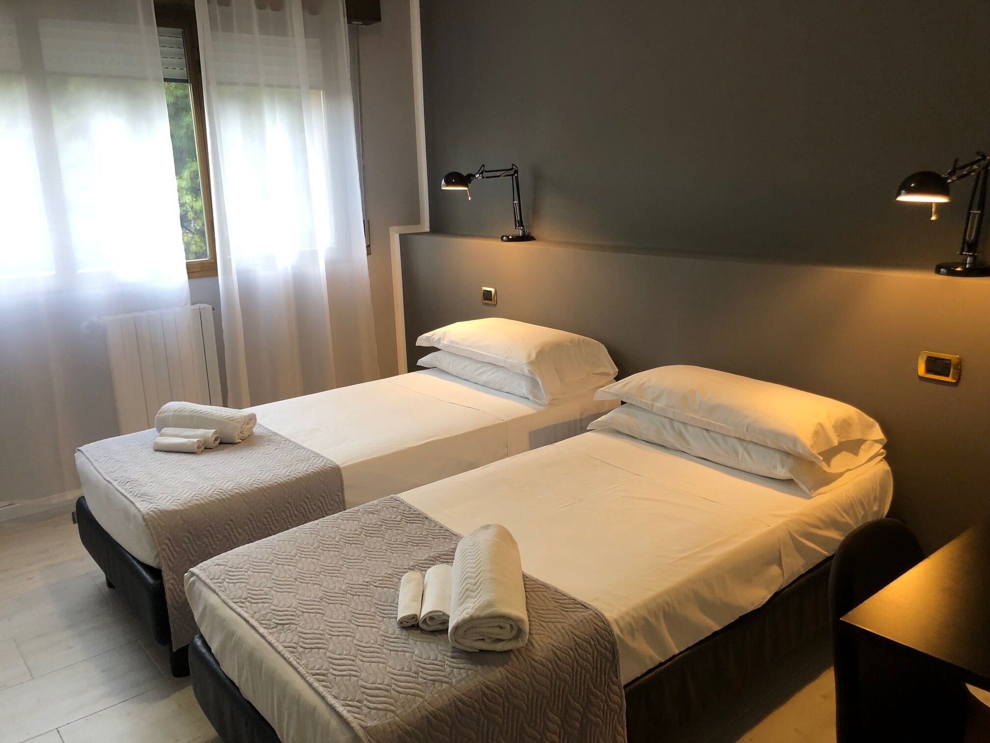 Une chambre d’hôtel avec deux lits simples, chacun agrémenté d’une serviette roulée, de lampes de chevet et d’une fenêtre avec des rideaux légers.