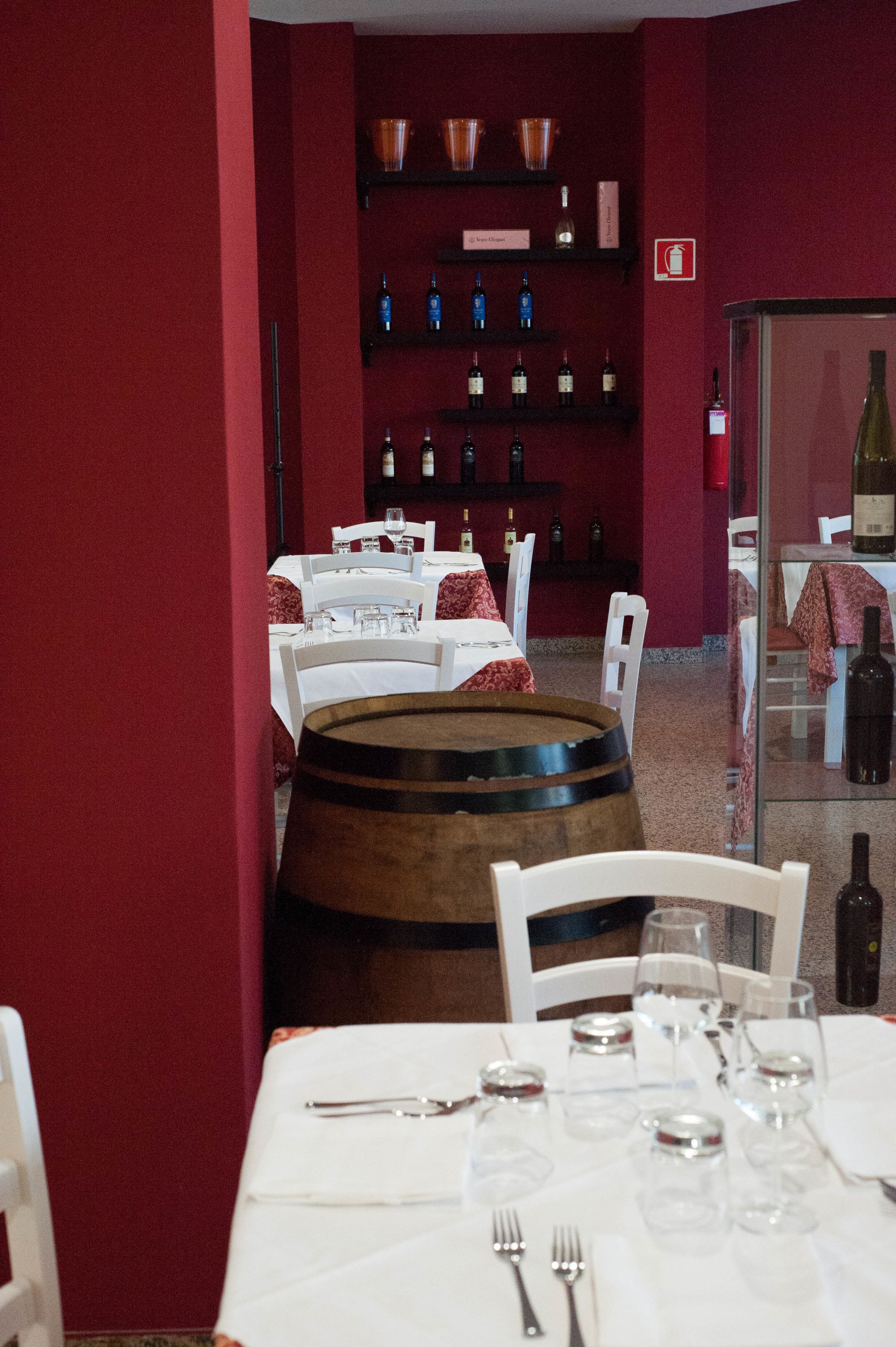 A restaurant with tables set for dining, a wine rack with bottles, and a barrel in the foreground.
