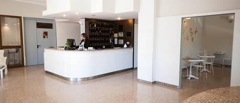 A modern reception area with a white counter, a bar area, and seating.