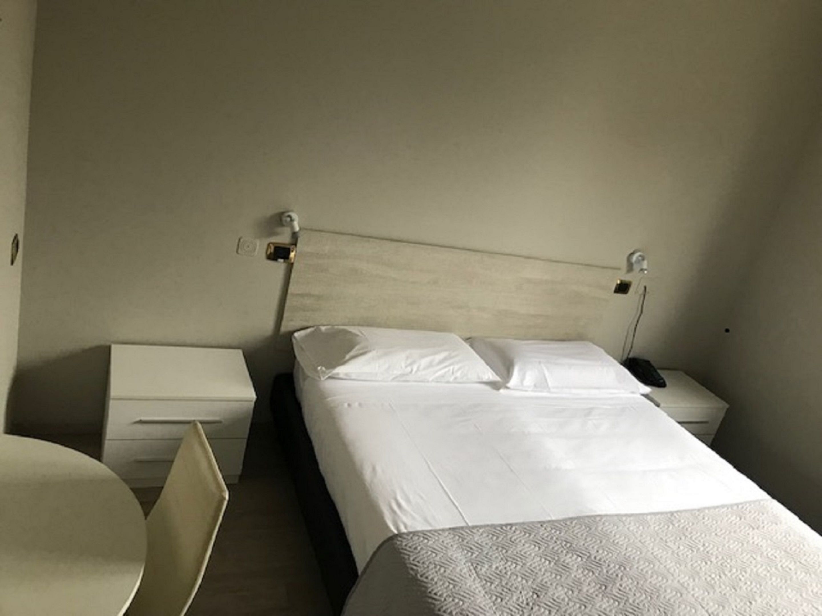 Et simpelt, rent hotelværelse med seng, sengeborde og et lille rundt bord.