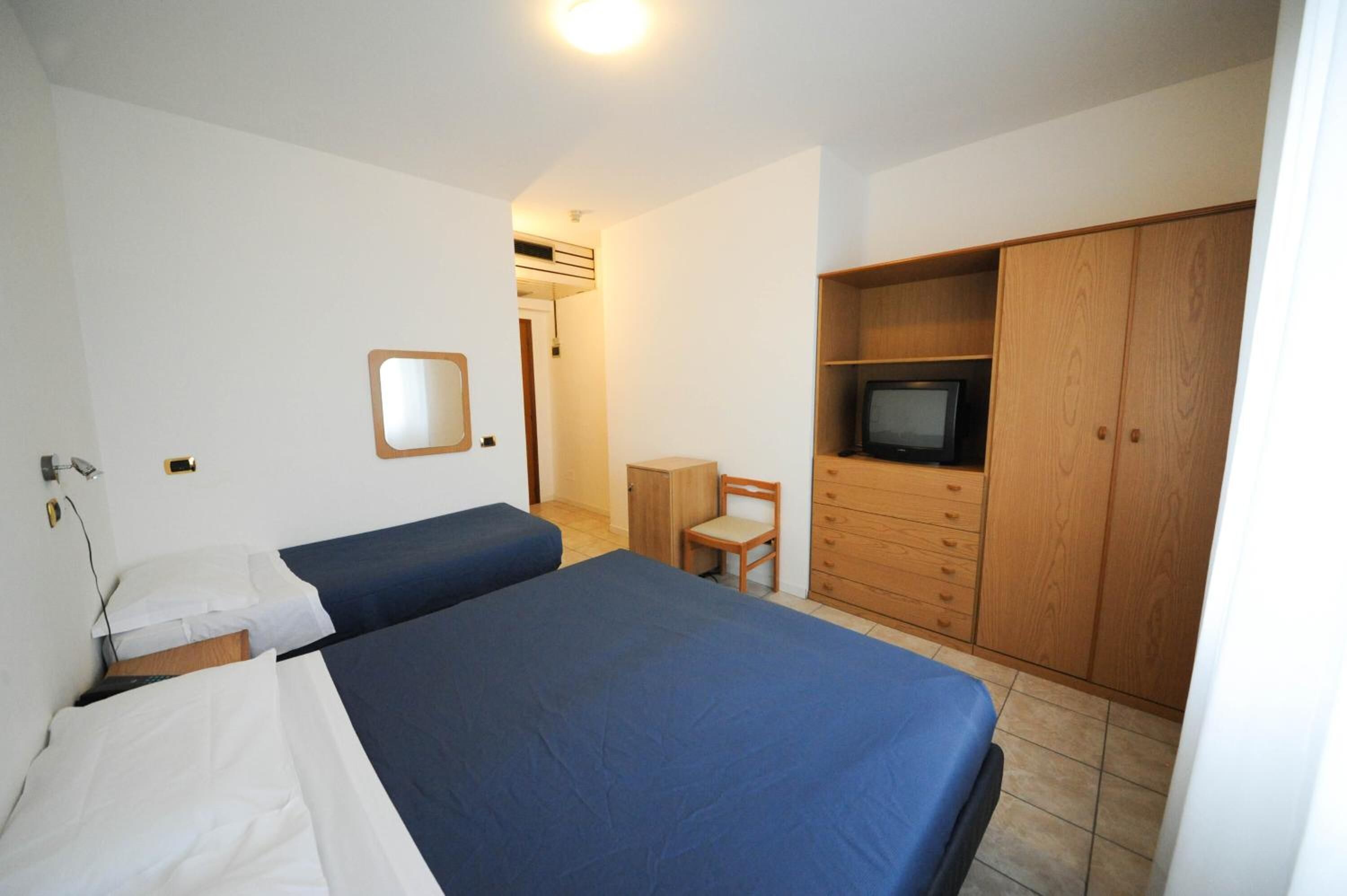A bedroom with two beds, a wooden wardrobe, a television, and a small cabinet.