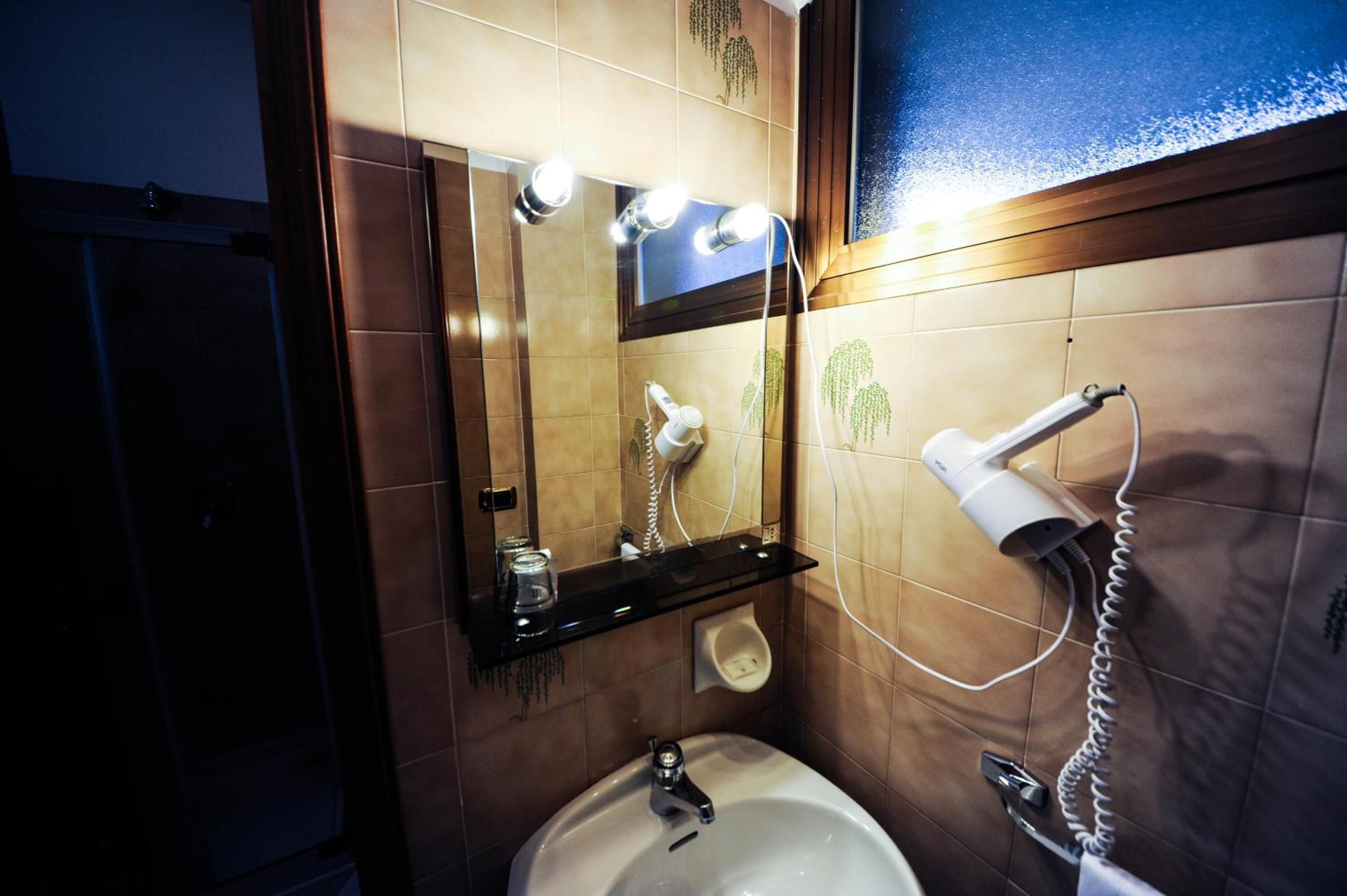A bathroom with a sink, mirror, hairdryer, and a shelf with a cup and a tissue box.