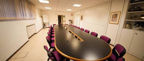 Une salle de conférence avec une longue table et des chaises violettes, des murs blancs et un sol carrelé.
