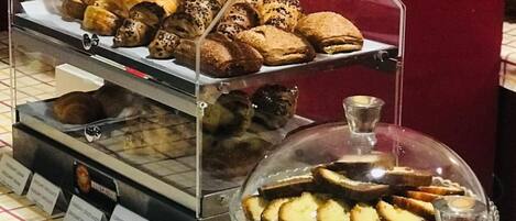 A bakery display with various pastries and cakes, including a sign for 'PLUM CAKE CACAO'.