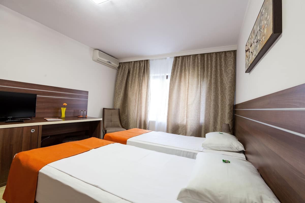 Habitación de hotel con dos camas, un escritorio, un televisor y una ventana con cortinas.