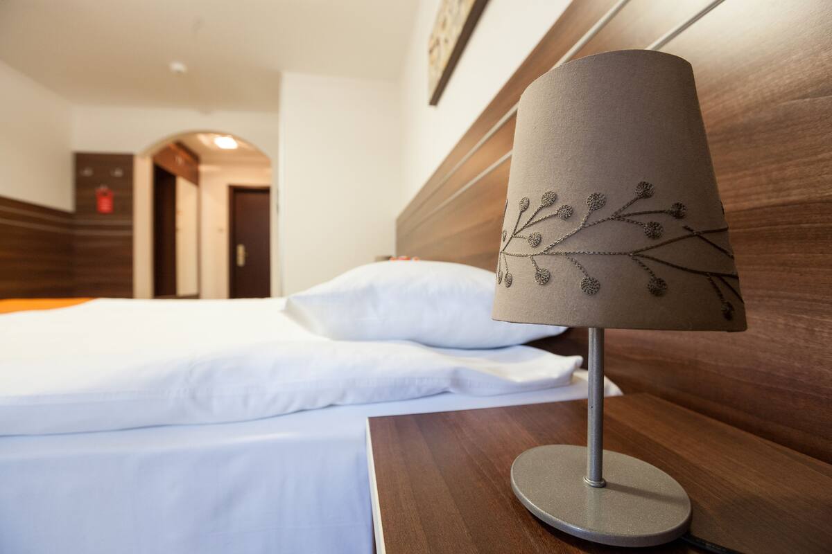 Una cama bien hecha con sábanas blancas, cabecera de madera y lámpara con diseño de rama.