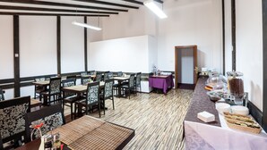 A dining area with tables and chairs, a buffet with various food items, and a wooden ceiling with exposed beams. - Hotel Citadella Bucuresti (Bucharest)