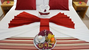 Una cama bien hecha con una toalla dispuesta en forma de corazón, una bandeja con alimentos para el desayuno y almohadas rojas.
