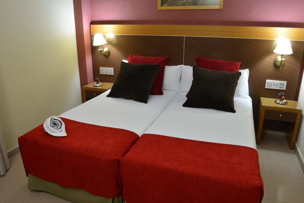 Ein Doppelbett mit roter und weißer Bettwäsche, zwei Nachttischlampen und ein Holz-Kopfteil.