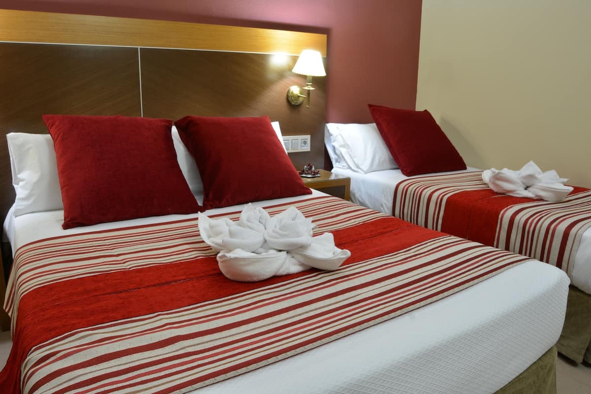 Ein Hotelzimmer mit zwei Betten, jeweils mit rot-weiß gestreifter Bettwäsche, und einem Kopfteil mit einer Leuchte.